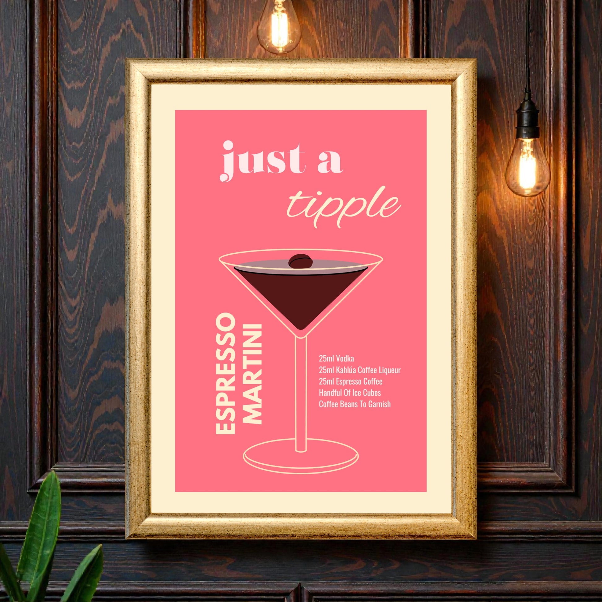 Framed espresso martini cocktail recipe wall art featuring a minimalist illustrated martini glass on a pink background with the text “Just a tipple Espresso Martini,” styled against a dark wood wall with warm hanging lights.