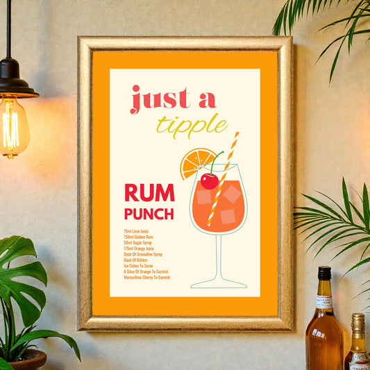 Framed rum punch cocktail recipe print with orange border, illustrated drink glass, and tropical decor displayed on a wall with plants and bar accessories.