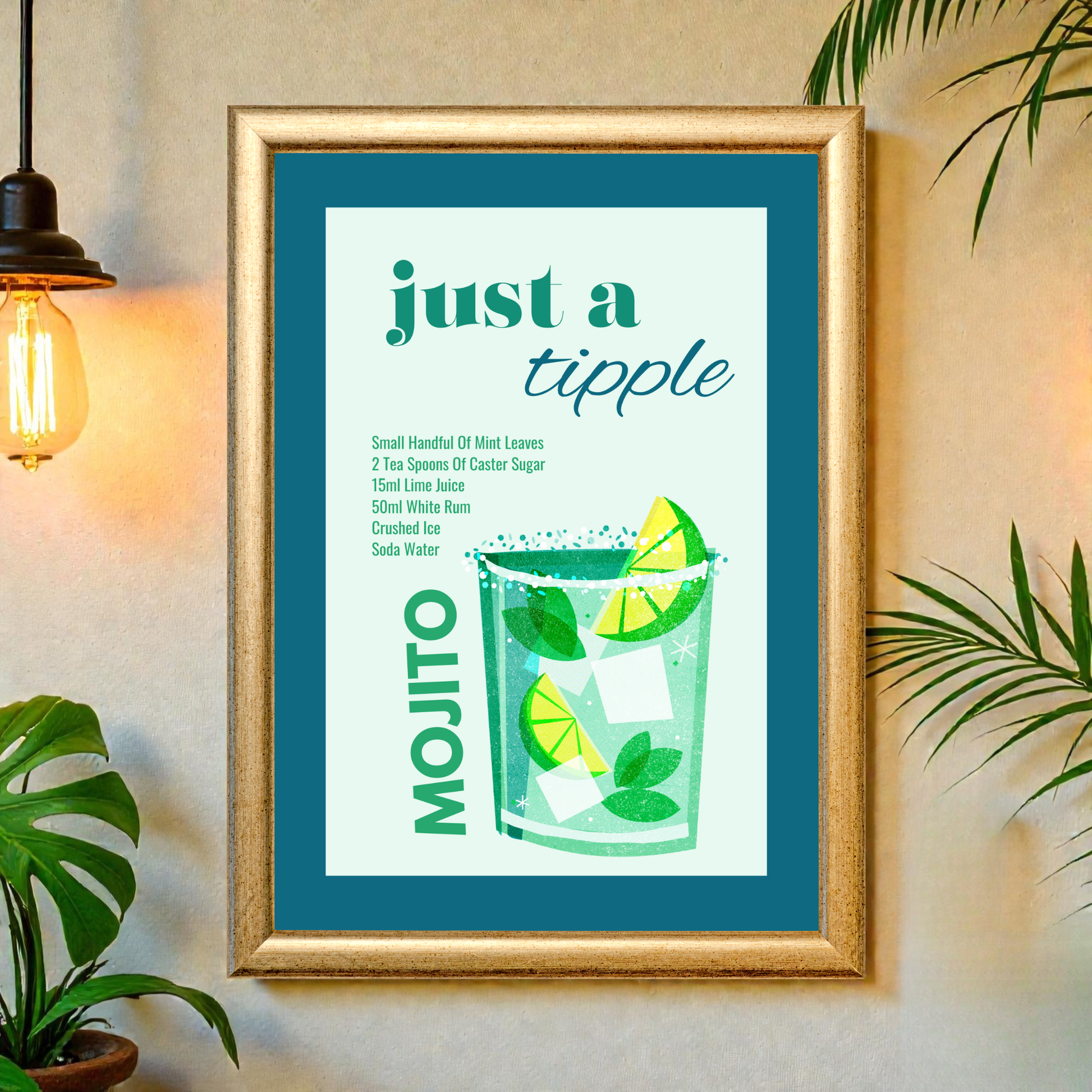 Framed “just a tipple – Mojito” cocktail print displayed on a wall in a cozy interior setting with plants and a warm wall light. The artwork shows a green mojito with lime slices, mint leaves, ice cubes, and the recipe printed alongside inside a wooden frame.