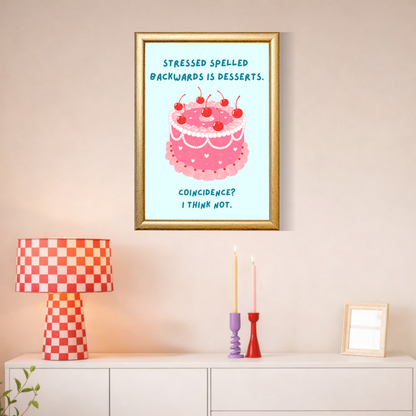 Framed artwork with a cake illustration and text on a wall above a cabinet with decorative items.